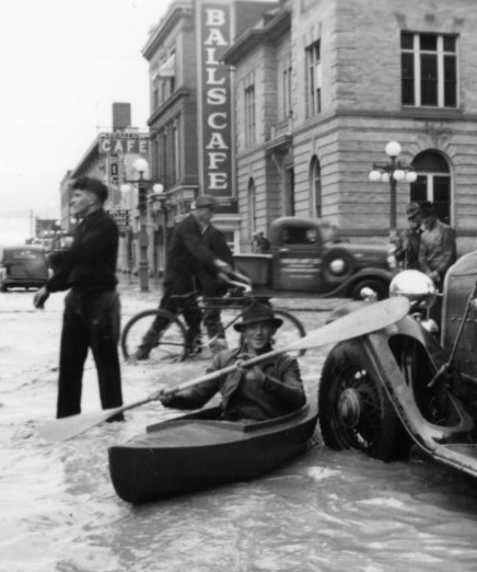 Person in a canoe paddling down a main street downtown during a flood